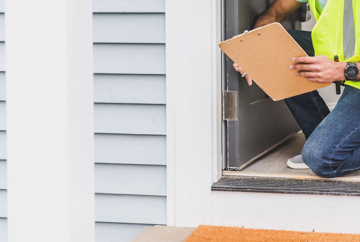 A home inspector wearing safety gear examines a house interior for safety compliance.